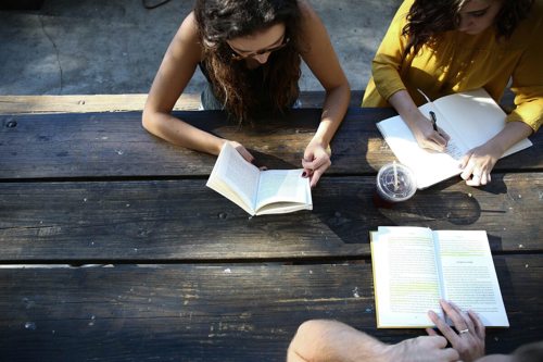 An aerial view of three students studying books together on a bench.