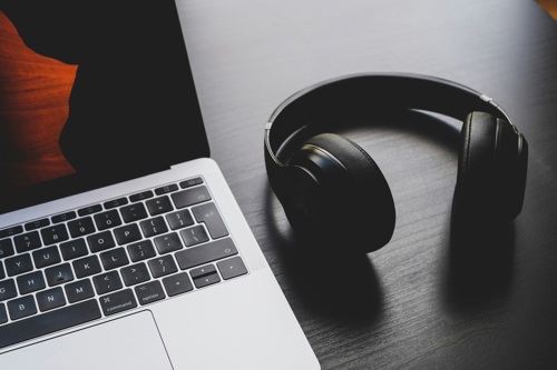 A pair of black headphones rest beside a laptop on a desk.