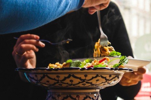 A close-up of a blue and white dish full of noodles and vegetables.