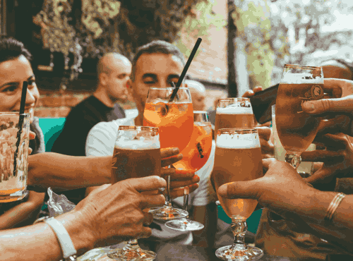 A group of friends all cheers their pints in pub searing area with natural lighting