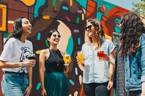 Four friends talk and laugh over drinks in front of a colourful mural.