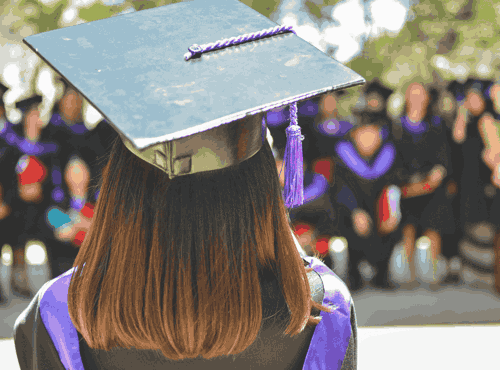 A girl in a purple and black graduation gown and cap looking at fellow graduates
