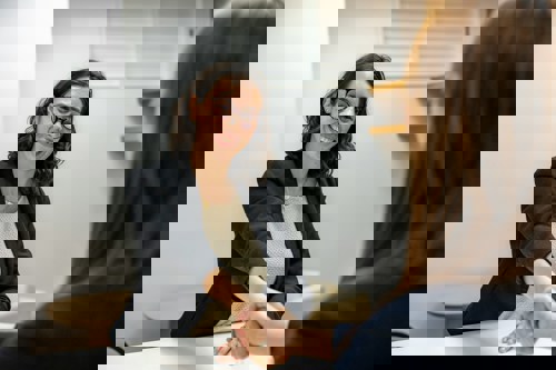 two women in business attire shaking hands over a desk