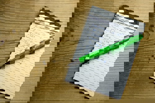 Shopping list on note pad with green pen laying on the pad