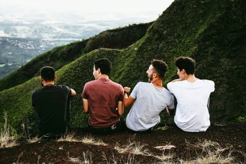 Four young male students laugh together on top of a hill.