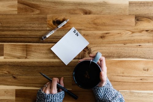 An aerial view of a desk as a woman outlines her goals on a 'To Do' List with a hot drink.