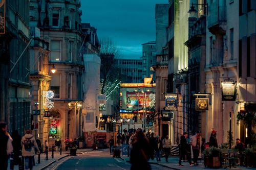 People walk down a pleasant Bristol high street at night.