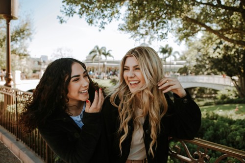 Two girl friends laugh and walk in the park together.