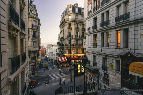 Pedestrians stroll down a Parisian street in the city with tall grand buildings either side.
