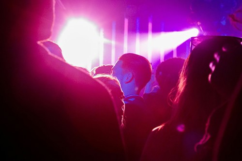 Silhouettes of clubbers dance under pink and purple lighting.